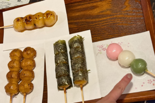 Assorted Japanese skewered sweets: grilled sesame-dango, fried dango balls, and seaweed-wrapped dango on sticks, with pastel mochi on the side.