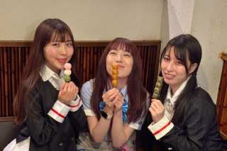 Three young women smile and hold colorful skewered dumplings (dango) at a casual eatery, posing for a photo.